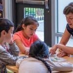 A teacher talks with three young students at a table.